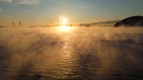 Aerial-Low-Flying-Over-Waves-With-Floating-Mist,-Tilt-Up-To-Reveal-Golden-Hour-Sunset-Near-Bjorvika,-Oslo