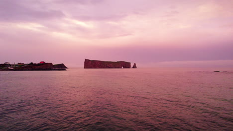 Drone's-backward-view-of-Percé-Rock-during-a-cloudy-sunset
