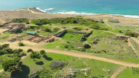 Tourists-visiting-Tombs-of-the-Kings-in-Paphos,-Cyprus,-aerial-parallax-shot