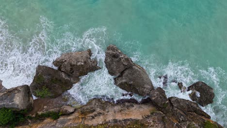 Large-boulders-from-tropical-island-on-coast-bombarded-by-rough-winter-swell-in-ocean,-drone-top-down