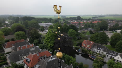 Aerial-view-orbiting-ornate-metal-cockerel-weather-vane-lightning-conductor-cross-overlooking-charming-Dutch-village