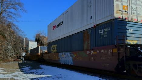 Una-Toma-De-ángulo-Bajo-De-Un-Largo-Tren-De-Carga-Con-Una-Carga-Completa,-Cubierto-De-Graffiti-En-Un-Día-Soleado-Con-Cielos-Azules-Y-Despejados