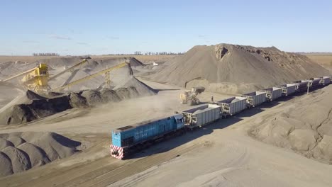 Freight-train-being-loaded-at-a-vast-industrial-mining-site,-under-clear-skies