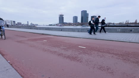 Eine-Person-Fährt-Mit-Einem-Motorrad-Auf-Einem-Ausgewiesenen-Fahrradweg-Auf-Einer-Brücke,-Während-Fußgänger-In-Der-Nähe-Unterwegs-Sind.-Dies-Veranschaulicht-Die-Mischung-Aus-Moderner-Mobilität-Und-Aktivem-Lebensstil-Der-Stadt-Vor-Einer-Städtischen-Kulisse