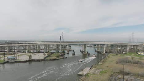 Una-Vista-Aérea-Captura-El-Barco-De-Respuesta-De-Emergencia-Firestorm-70-Del-Departamento-De-Bomberos-Del-Puerto-De-Houston-Pasando-Por-Debajo-Del-Puente-Kemah-Y-Entrando-Al-Lago-Clear-En-Kemah,-Seabrook,-Texas.