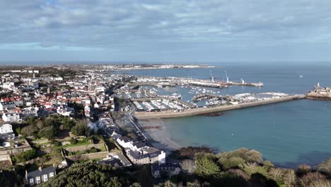 St-Peter-Port-Guernsey-flight-tracking-seafront-from-Havelet-Bay,-showing-Castle-Breakwater-and-marinas-with-views-over-Belle-Greve-Bay-on-bright-sunny-day-with-calm-clear-sea-and-blue-sky