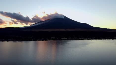 Majestic-Mount-Fuji-at-sunset,-reflected-in-a-tranquil-lake-with-silhouette-of-landscape