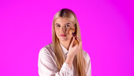 European-woman-looking-at-camera-and-applying-makeup-with-cosmetic-brush