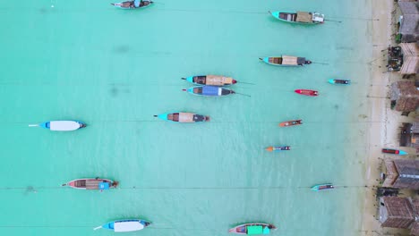 Long-Tail-Boats-with-an-Aerial-Top-Down-Panning-Shot-to-Reveal-Wooden-Huts-Along-a-Beach-in-Thailand