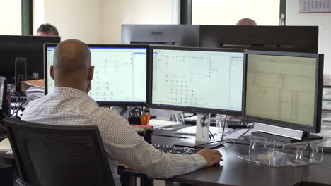 Bald-office-employee-looking-at-screens-while-sitting-behind-his-desk,-zoom-out