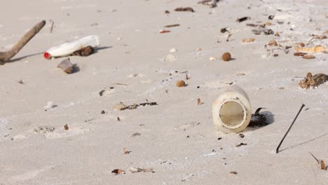 Playa-Llena-De-Residuos-Plásticos-Esparcidos-Por-La-Arena,-Destacando-La-Contaminación-Ambiental