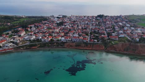 Vista-Aérea-De-Potidea,-Una-Ciudad-Costera-En-Grecia,-Chalkidiki,-Con-Aguas-Cristalinas-Y-Verdes-Del-Mar-Egeo