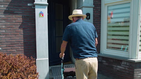Back-view-of-aged-pensioner-man-unlocking-automatic-home-door-with-remote-device