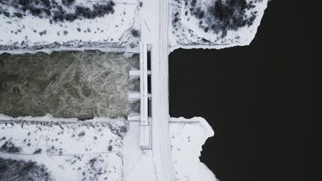 Große-Höhe-Von-Oben-Nach-Unten-Luftaufnahme-Rauschendes-Wasser-Notigi-Kontrollstruktur-Staudamm-Fluss-See-Verschneite-Landschaft-Nördlichen-Winter-Manitoba-Kanada