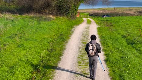 Rückansicht-Eines-Mannes,-Der-Ein-Stativ-Trägt,-Während-Er-Auf-Einem-Feldweg-Geht