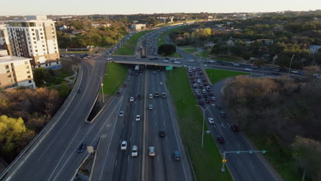 Vista-Aérea-De-Un-Bullicioso-Paisaje-Urbano:-Tráfico-Intenso-En-La-Intersección-Con-Una-Mezcla-De-Automóviles-Y-Camiones-En-Una-Autopista-De-Varios-Carriles