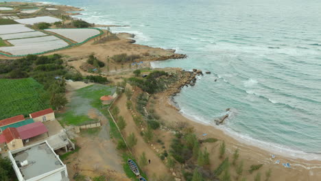 Aerial-view-of-Kapparis-in-Paralimni,-Cyprus,-reveals-a-serene-coastal-area-where-agricultural-fields-meet-the-sandy-beach-and-rocky-shoreline,-with-the-Mediterranean-Sea-stretching-into-the-horizon