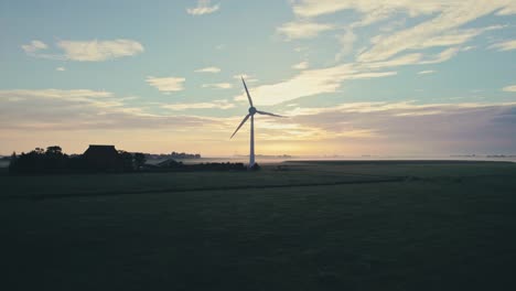 Wind-turbine-spinning-in-silhouette-against-a-vibrant-sunrise,-rural-setting-with-clear-horizon