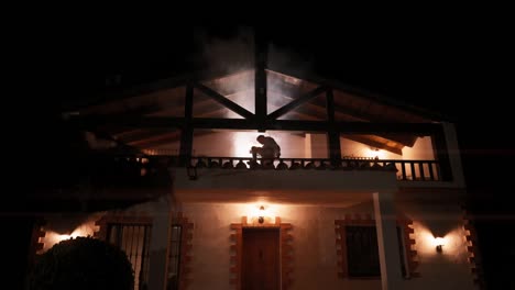 A-man-climbs-over-the-railing-of-a-house-at-night-as-white-smoke-blows-out