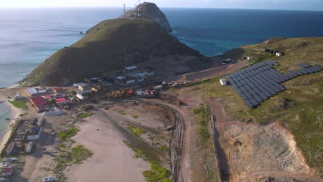Aerial-View-of-Construction-Site-with-Solar-Panels-on-Hilltop-Near-Ocean,-Caribbean-island