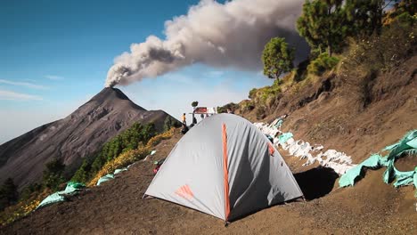 Der-Blick-Von-Einem-Campingplatz-Zeigt-Den-Vulkan-Fuego,-Der-In-Unmittelbarer-Nähe-Der-Zelte-Ausbricht-Und-Den-Himmel-Mit-Einer-Großen-Dunklen-Aschewolke-Bedeckt