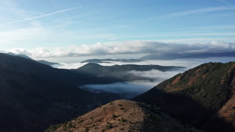 La-Luz-De-La-Mañana-Baña-El-Paisaje-Montañoso,-Con-Valles-Envueltos-En-Niebla-Y-Un-Cielo-Azul-Claro,-Una-Serena-Vista-Aérea