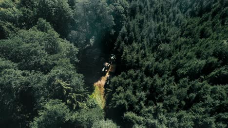 Traktoren-Auf-Einem-Waldweg,-Umgeben-Von-Dichten-Grünen-Bäumen-Bei-Tageslicht,-Luftaufnahme