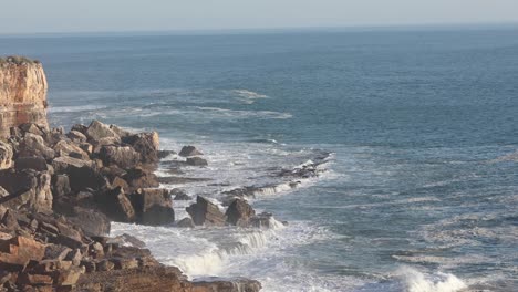 Aerial-drone-view-over-waves,-storming-the-coast-of-sunny,-golden-hour-Portugal