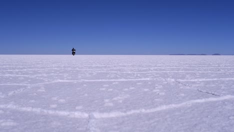 Motorcycle-rides-toward-low-angle-camera-on-Uyuni-Salt-Flat,-Bolivia