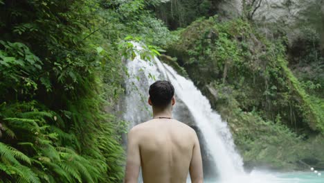 Un-Joven-Blanco-Musculoso-Se-Para-Frente-A-Las-Cataratas-Kawasan-Levantando-Los-Brazos-Para-Disfrutar-De-Vistas-épicas.