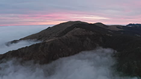 Misty-mountain-peaks-at-dusk-with-soft-pink-skies,-aerial-view