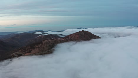 Majestic-mountains-peaking-through-a-serene-sea-of-clouds-at-dusk,-evoking-tranquility,-aerial-view