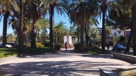 Boy-rides-kickbike-scooter-in-park-with-fountain-in-Antibes,-France