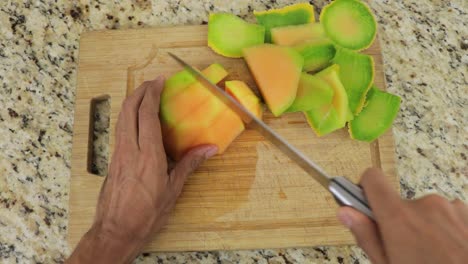 Cutting-juicy-and-sweet-melon-into-cubes-with-knife-on-cutting-board,-POV