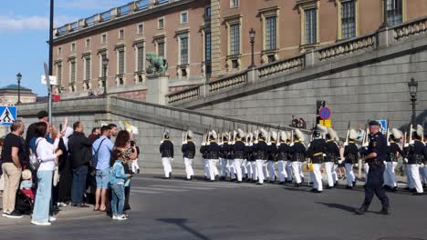 Royal-guards-marching-by-Swedish-Royal-Palace-on-National-Day,-spectators-line-streets