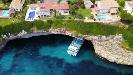 Pedestal-descending-drone-shot-of-Cala-Anguila,-revealing-some-residential-mansions-and-guest-houses-above-an-underground-cave-located-in-the-island-of-Mallorca