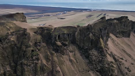 Aerial-view-of-a-scenic-cliff-on-a-mountain-in-Iceland,-with-a-dramatic-evening-cloudscape-and-flying-birds