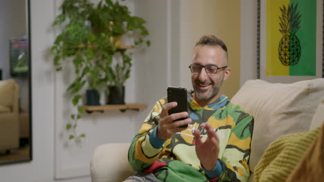 Man-relaxing-on-the-couch,-finds-amusement-in-what-he-reads-on-his-smartphone