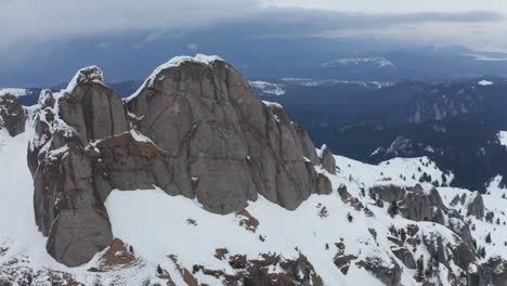 Aerial-shot-of-snow-capped-Ciucas-Mountains-against-cloudy-sky,-dramatic-winter-landscape