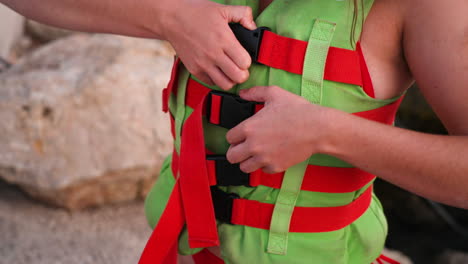 Young-anonymous-female-opening-life-jacket-buckle-to-reveal-red-bikini-swimwear-outfit