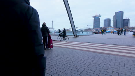 Eine-Geschäftige-Urbane-Szene-Vor-Einem-Modernen-Verkehrsknotenpunkt,-Mit-Fußgängern,-Einem-Radfahrer-Und-Einem-Arbeiter-In-Einer-Warnweste,-Mit-Der-Skyline-Der-Stadt-Im-Hintergrund