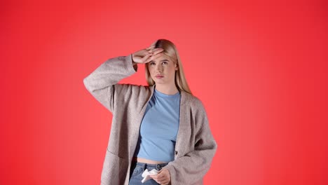 Young-woman-with-fever,-blows-nose-in-napkin,-isolated-red-background,-studio