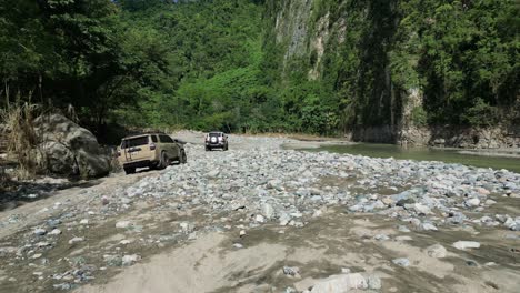 Off-road-cars-driving-along-shores-of-river-at-Muchas-Aguas,-Dominican-Republic