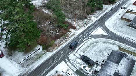 Overhead-view-of-a-black-car-driving-through-snow-covered-rural-streets