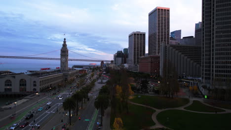 San-Francisco-USA,-Aerial-View-of-Historic-Ferry-Building,-Bay-Trail-Traffic,-Embarcadero-Plaza-Buildings-After-Sunset,-Drone-Shot