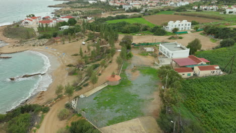 Coastal-Beachfront-Agricultural-Farms-With-Orange-Roof-Buildings-by-the-Sea-in-Cyprus---Aerial-Flyover