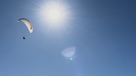 A-single-para-glider-flying-across-the-bright-sun-on-a-beautiful-day-at-Torrey-Pines-Gliderport,-in-La-Jolla,-California