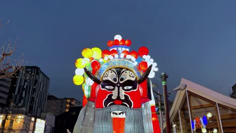 Large-traditional-Japanese-mask-display-with-lanterns-at-dusk,-vibrant-cultural-event