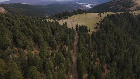 SUV-drives-along-dirt-road-between-tall-forested-mountain-pass-up-above-Agrafa,-drone-tracking