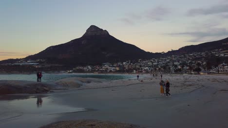 Touristen-Am-Strand-In-Der-Camp-Bay-In-Der-Abenddämmerung-Mit-Löwenkopf-Im-Hintergrund